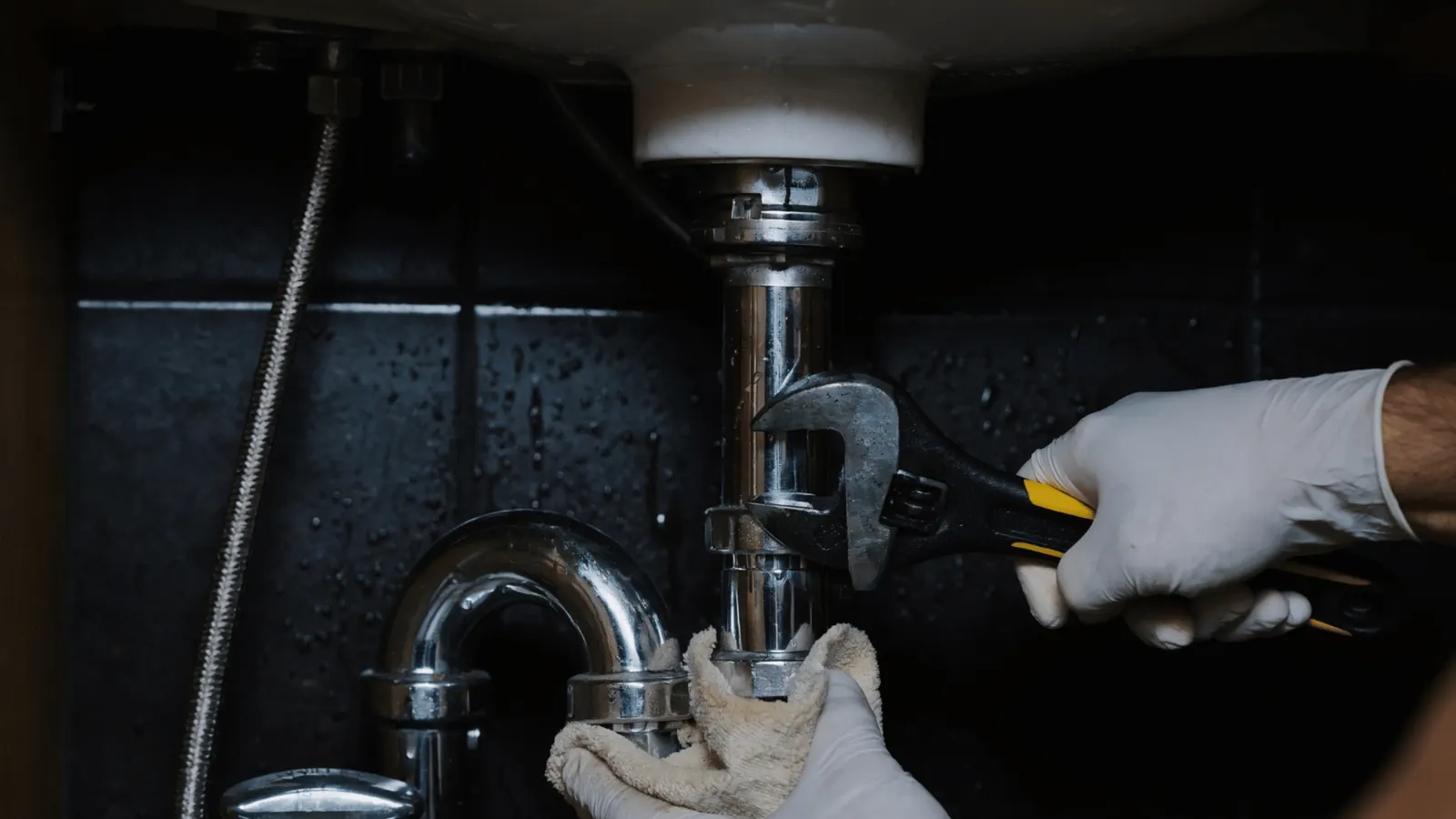 Plumbing technician tightening a copper pipe connection under a sink